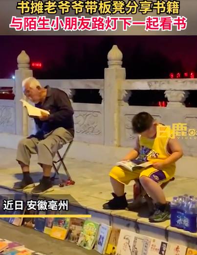 小朋友与书摊爷爷路灯下默契看书 一个探索未来一个品味过去