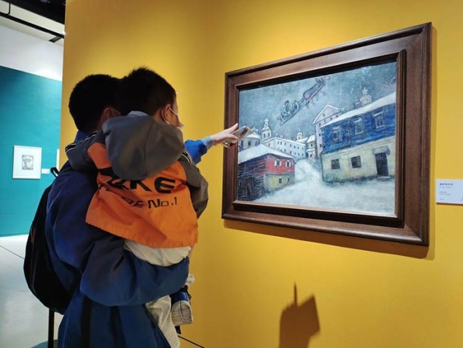 观众在欣赏夏加尔1929年布面油画作品《俄罗斯村庄》。
