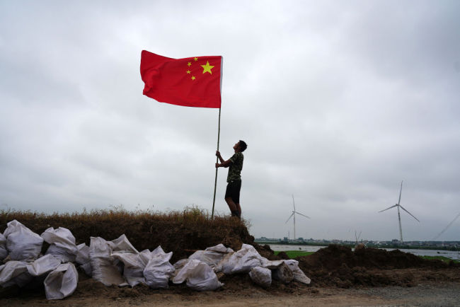 7月16日，在江西省九江市，退役军人张恒扶正防洪哨所门前的国旗。洪水来袭，曾服役于天安门国旗护卫队的张恒同父亲一起投身防汛抗洪战斗。他说，过去我护卫的是国家的荣誉和尊严，现在我守卫的是父母和家乡。新华社记者 周密 摄