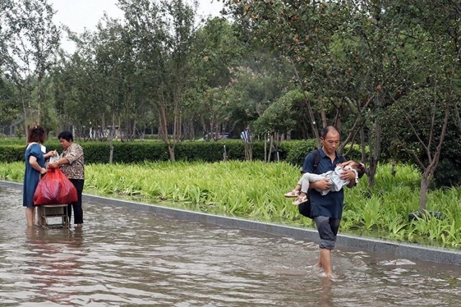 7月21日，郑州，在外避雨的居民抱着熟睡的孩子准备返家。