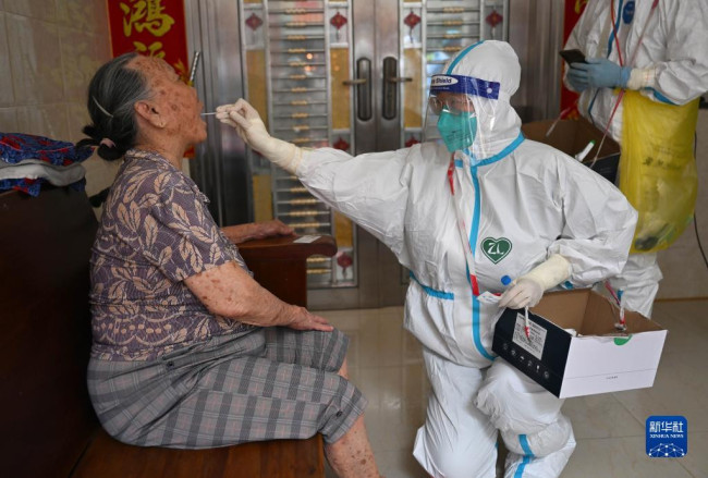 8月11日，河南省援海南三亚医疗队的医护人员李娟（右）在三亚市天涯区南边海渔村为行动不便的老人进行入户核酸采样。