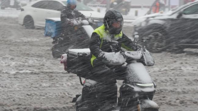 外賣小哥暴雪中緩慢前行送餐 濕滑路面艱難騎行