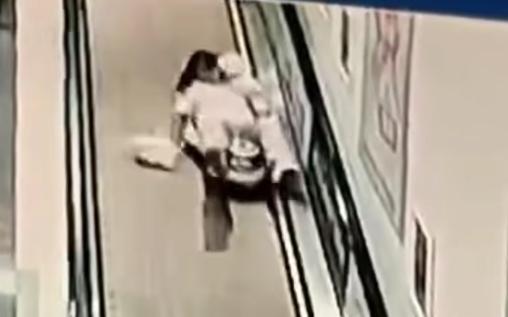 女子怀抱婴儿在扶梯上被撞倒